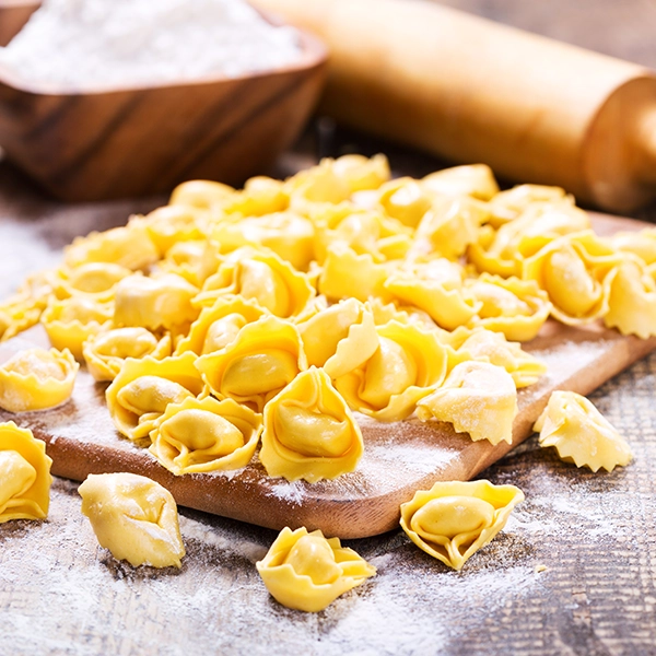 Tortellini fatti a mano su un tavolo con farina e matterello in sfondo